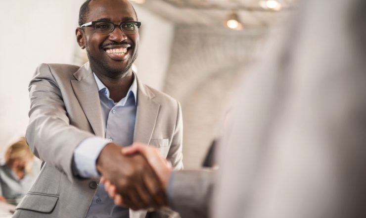 Happy African American businessman shaking hands with his unrecognizable colleague.